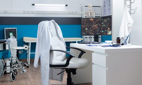 Computer with covid19 illustration on screen standing on desk in empty office room during global pandemic. Modern hospital room equipped with professional medical instruments. Virus cell image